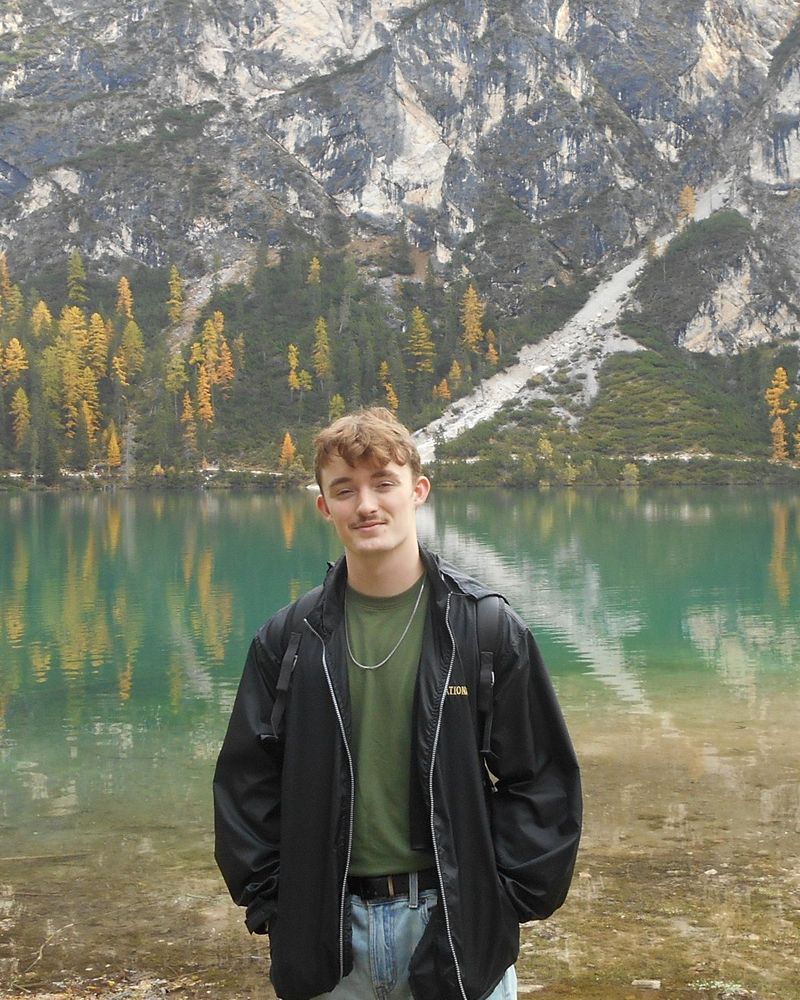 Caden Drover standing by a mountain lake with autumn larch trees behind him